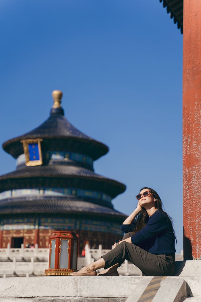 Mujer sentada, mirando al cielo, de fondo un hermoso templo Chino