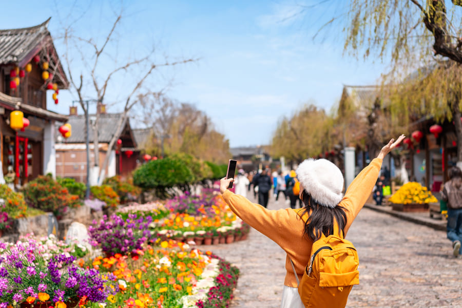 Turista con los brazos abierto apreciando la belleza de Yunnan China, al fondo personas caminando y flores de muchos colores
